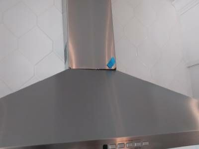 A stainless steel range hood and its vent shaft against hexagonal white tile, viewed from below