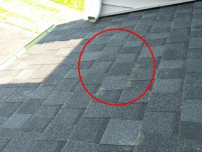 Asphalt shingles on a porch roof, with a red circle around a patch of damaged, caulked shingles